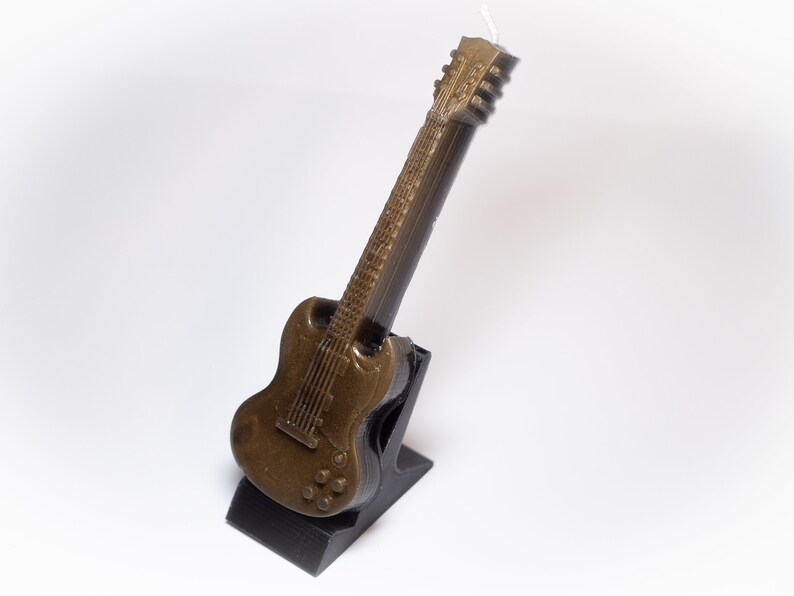May include: A brown guitar-shaped candle on a black stand. The candle is detailed with a textured finish and a black pickguard.