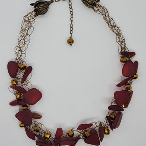 May include: A necklace with a bronze-colored chain and a series of dark red, irregularly shaped beads. The necklace also features small, gold-colored beads and decorative bronze-colored floral accents.