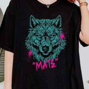 May include: Black t-shirt with a teal wolf graphic and pink paint splatters. The text "MATS" is printed in pink below the wolf.