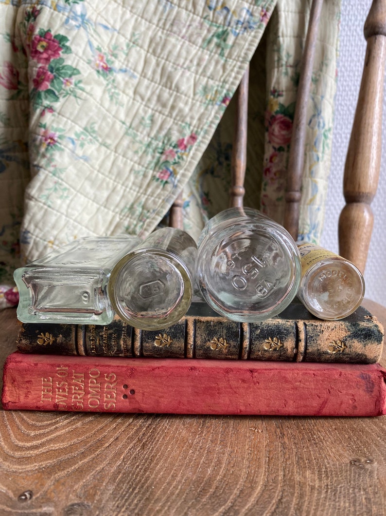 Op de afbeelding: Vier heldere glazen flessen met kurkstoppen gestapeld op drie vintage boeken. Het bovenste boek is rood en heeft gouden letters met de tekst "The Lives of Great Composers Series".