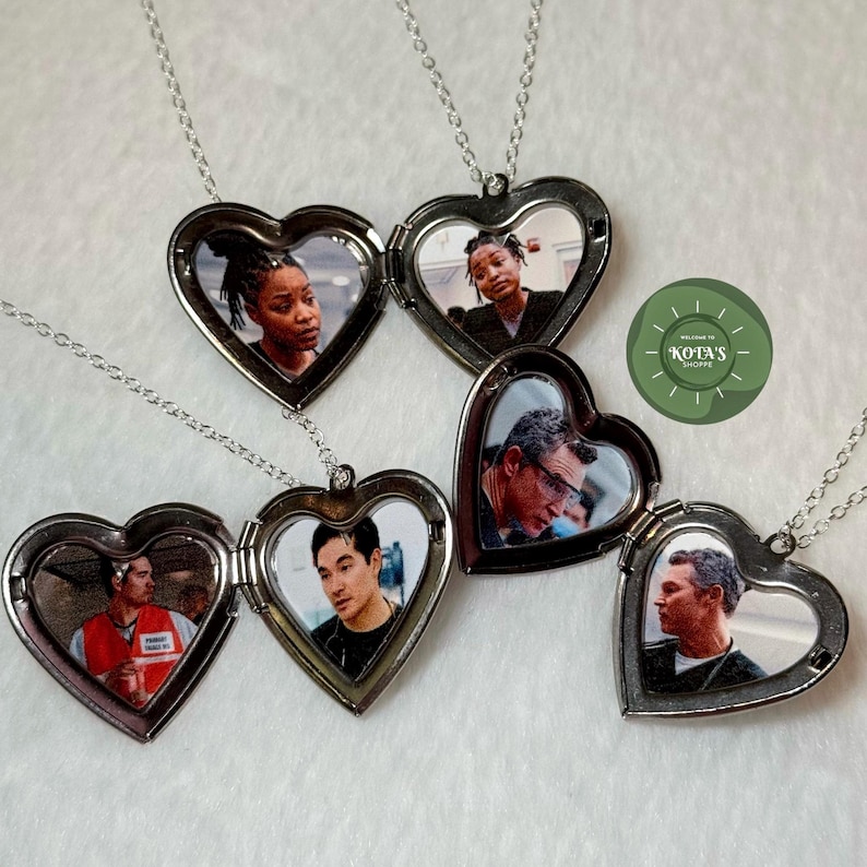 May include: Heart-shaped silver lockets with photos inside, hanging on delicate silver chains. The lockets are open, revealing the images of people. The background is a soft, white surface. The shop's logo is visible in the image.