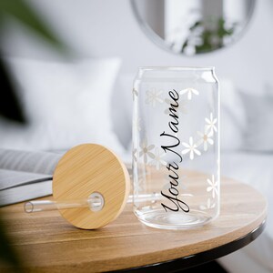 Könnte beinhalten: Ein klares, dosenförmiges Glas mit Bambusdeckel und Strohhalm. Das Glas ist mit einem Blumenmuster und dem Text "Your Name" verziert. Der runde Deckel ist aus hellfarbenem Bambus gefertigt.