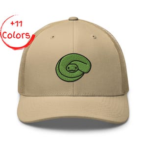 Könnte beinhalten: Eine beige Trucker-Cap mit Netzrücken und gebogenem Schirm. Auf der Vorderseite befindet sich eine Stickerei einer zusammengerollten grünen Schlange mit einfachem Gesicht. Der Text +11 Colors ist in Rot in der oberen linken Ecke abgebildet.