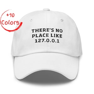 May include: White baseball cap with the text "THERE'S NO PLACE LIKE 127.0.0.1" in black. A red circle with the words "+10 Colors" is in the upper left corner. The cap has a curved brim and an adjustable strap.