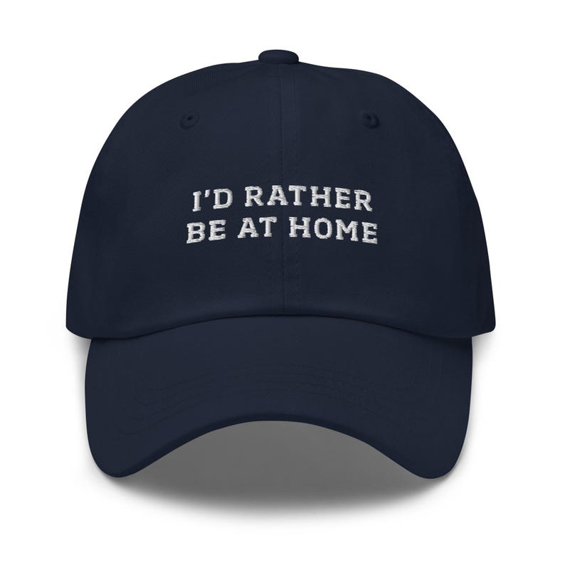 May include: Navy blue baseball cap with the embroidered text "I'D RATHER BE AT HOME" in white. The cap has a curved brim and a classic six-panel design, suitable for casual wear.