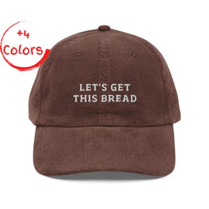 May include: A brown corduroy baseball cap with the embroidered text "LET'S GET THIS BREAD" in white. The cap has a curved brim and a rounded top. A red circle with the words "+4 Colors" is in the upper left corner.