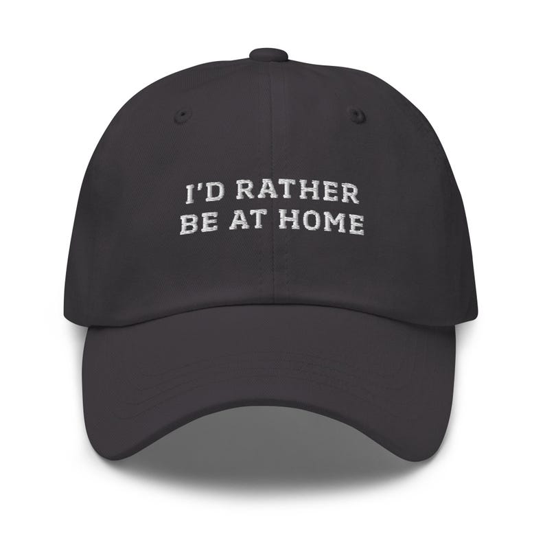 May include: A dark gray baseball cap with the embroidered text "I'D RATHER BE AT HOME" in white. The cap has a curved brim and a structured fit, suitable for casual wear.