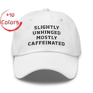 May include: White baseball cap with the text "SLIGHTLY UNHINGED MOSTLY CAFFEINATED" in black. The cap has a curved brim and a button on top. A red circle with the words "+10 Colors" is in the upper left corner.