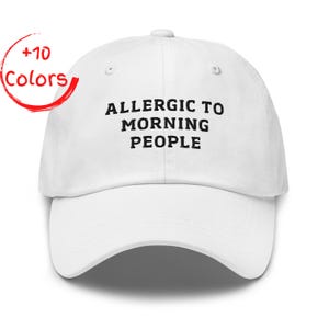 May include: White baseball cap with the text "ALLERGIC TO MORNING PEOPLE" in black. A red circle with the words "+10 Colors" is in the upper left corner. The cap has a curved brim and an adjustable strap.