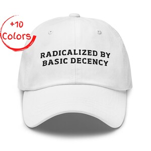 Op de afbeelding: Witte baseballpet met de tekst "RADICALIZED BY BASIC DECENCY" in zwart. De pet heeft een gebogen klep en een knoop aan de bovenkant. Een rode cirkel met de woorden "+10 Colors" staat in de linkerbovenhoek.