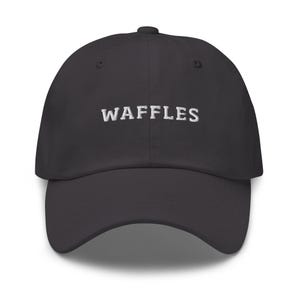 May include: A dark gray baseball cap with the word "WAFFLES" embroidered in white across the front. The cap has a curved brim and a structured crown.