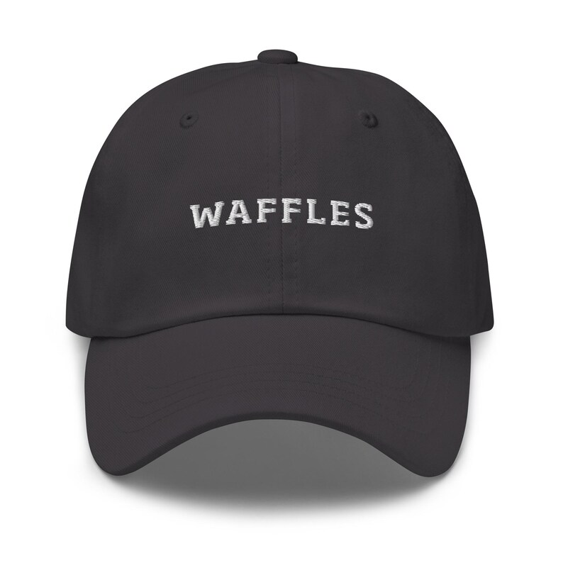 May include: A dark gray baseball cap with the word "WAFFLES" embroidered in white across the front. The cap has a curved brim and a structured crown.