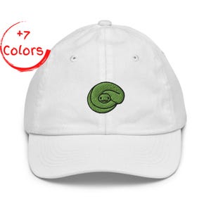 Może przedstawiać: Biała czapka bejsbolowa z zielonym haftowanym wzorem węża. Wąż jest zwinięty i ma szczegółową twarz. Tekst "+7 Colors" znajduje się w czerwonym okręgu po lewej stronie czapki.