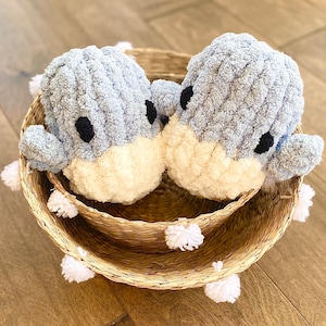 May include: Two blue and white plush toys shaped like birds in a woven basket with white pom-poms around the rim.