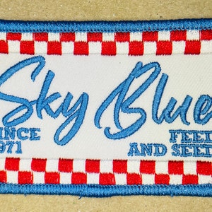 May include: Blue and white embroidered patch with the text "Sky Blue" in a cursive font. The patch also includes the text "Since 1971" and "Feed and Seed". The patch has a red and white checkered border.