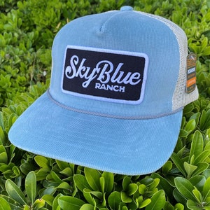 May include: A light blue corduroy trucker hat with a white mesh back. The hat has a black patch with white text that reads "Sky Blue Ranch".
