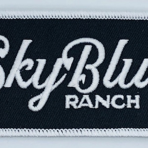 May include: White embroidered patch with the text "Sky Blue Ranch" on a black background.