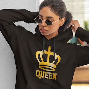 May include: Black hoodie with a gold crown graphic and the word "QUEEN" printed below. The hoodie has a drawstring hood and long sleeves. The graphic is centered on the front of the sweatshirt.