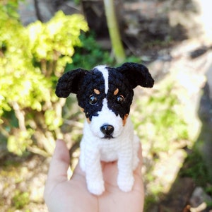 May include: A crocheted stuffed dog toy with black and white fur and brown eyes. The dog is sitting on a person's hand.