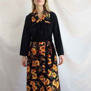 Puede incluir: Una larga bata de terciopelo negro con forro de estampado floral. La bata tiene cuello y cinturón de lazo. El estampado floral es en tonos naranja y amarillo.