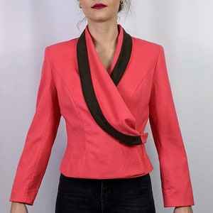 Puede incluir: Una chaqueta rosa con cuello negro y cierre cruzado. La chaqueta tiene mangas largas y una silueta ajustada.