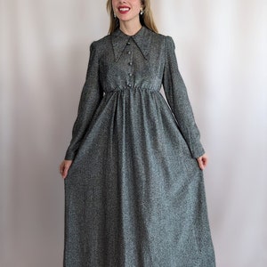 Könnte beinhalten: Ein langärmliges, graues Kleid mit einem großen, spitzen Kragen und Knopfverschluss. Das Kleid hat einen taillierten Oberteil und einen fließenden Rock.