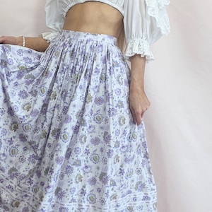 May include: A white and purple floral print midi skirt with a gathered waistband. The skirt has a white background with purple and green floral designs.
