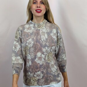 Puede incluir: Un suéter de color marrón y blanco con estampado floral, cuello alto y mangas 3/4.
