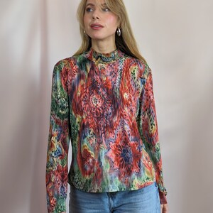 Puede incluir: Una camisa de manga larga y cuello alto con un estampado floral abstracto de colores. La camisa está hecha de una tela suave y elástica y tiene una silueta ajustada.