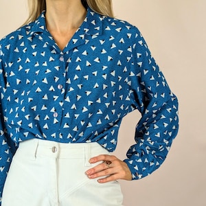 Puede incluir: Una camisa azul de manga larga con botones y un estampado geométrico blanco. La camisa tiene cuello y un corte holgado.