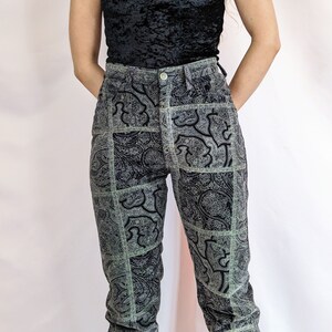 Puede incluir: Vaqueros de cintura alta con estampado paisley en negro y verde. Los vaqueros tienen una pierna recta y un corte holgado.