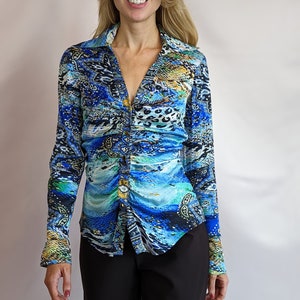 May include: A blue and black patterned long-sleeved shirt with a button-up front and a v-neck. The shirt has a gathered detail at the waist.