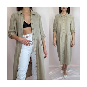 Puede incluir: Vestido camisero largo de lino beige. Presenta cuello camisero, mangas enrolladas y falda plisada. Botones dorados adornan el frente. El vestido llega aproximadamente a la rodilla.