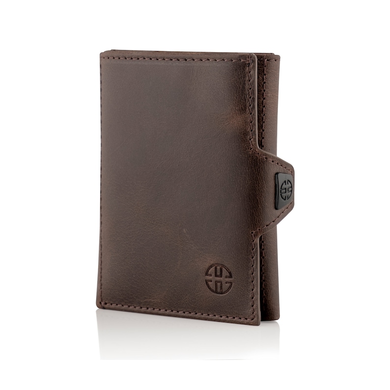 May include: A brown leather wallet with a flap closure and a small metal logo on the front. The wallet is folded in half and has a stitched edge.
