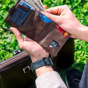 May include: A brown leather wallet with multiple card slots and a money clip. The wallet is open and shows a driver's license, credit cards, cash, and a memory card.