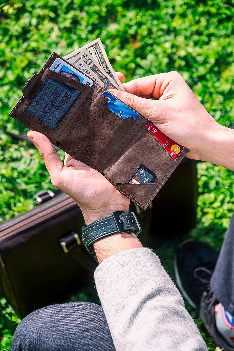 May include: A brown leather wallet with multiple card slots and a money clip. The wallet is open and shows a driver's license, credit cards, cash, and a memory card.