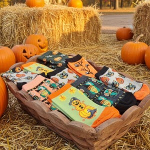 May include: A wooden basket filled with colorful Halloween-themed socks. The socks feature various designs, including pumpkins, scarecrows, and autumn leaves. The socks are displayed on a bed of hay, surrounded by pumpkins and hay bales.