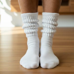 May include: A pair of white slouch socks featuring a ribbed knit texture that extends from the ankle to the mid-calf. The socks are made of a soft, opaque fabric and are designed to be worn bunched up around the lower leg for a relaxed fit.
