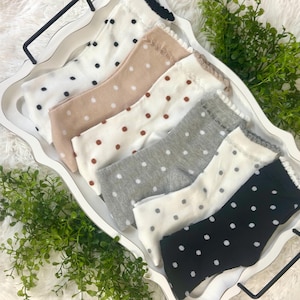 May include: A collection of six pairs of socks with a polka dot pattern, arranged in a white tray. The socks come in various colors, including white, beige, brown, gray, and black. Each pair features a different color of polka dots.