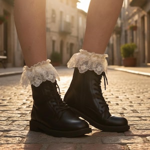 May include: A pair of black lace-up ankle boots featuring a smooth finish and rounded toes, paired with cream-colored ankle socks that have a wide, decorative lace ruffle trim extending above the top of the boot collars.