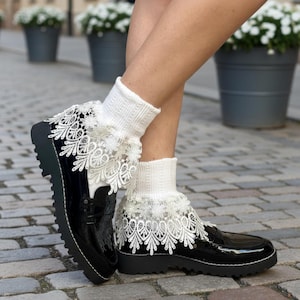 May include: Black patent leather loafers with a chunky sole, paired with white knit socks featuring delicate lace trim. The shoes have a glossy finish and a classic design.