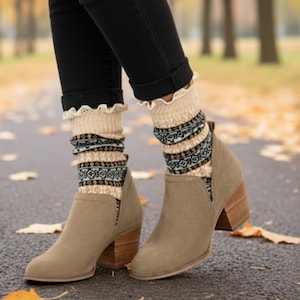 Könnte beinhalten: Taupefarbene Wildleder-Ankle Boots mit einem Holzblockabsatz. Dazu werden gemusterte Socken in Creme, Schwarz und Türkis getragen. Die Socken haben eine dekorative Spitzenborte. Die Person trägt eine schwarze Hose.