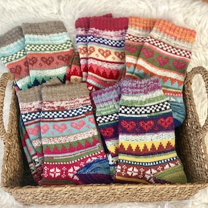 May include: A wicker basket filled with colorful, patterned socks. The socks feature heart and geometric designs in shades of red, blue, green, and yellow. The socks are made of a thick, knitted material, perfect for keeping feet warm.