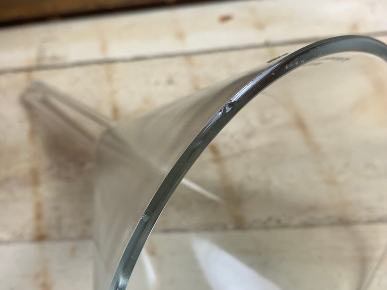May include: A clear glass funnel with a wide top and a narrow spout. The funnel is made of thick glass and has a smooth, polished finish.