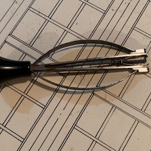 Può includere: Uno strumento per aprire la cassa dell'orologio con un manico nero e componenti metallici color argento. Lo strumento ha bracci curvi e un meccanismo per aprire le casse degli orologi. Lo strumento è su una superficie a motivi.