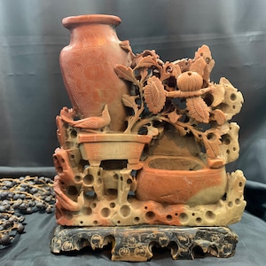 Peut inclure: Sculpture en pierre rouge sculptée à la main d'un vase avec un motif floral. La sculpture est sur une base en bois noir.