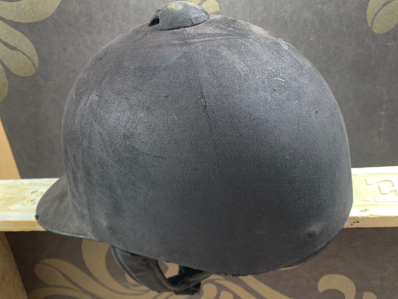May include: A black riding helmet with a smooth, slightly textured surface. The helmet has a small, round vent on the top.