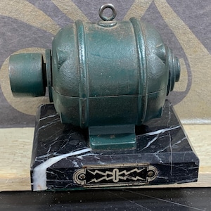 Op de afbeelding: Een kleine, groene, gietijzeren elektromotor op een zwarte marmeren basis met een wit bliksemontwerp.
