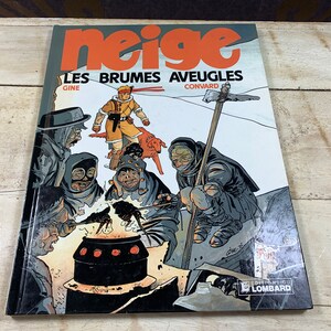 May include: A comic book cover with the title "Neige: Les Brumes Aveugles" by Gine and Convard. The cover features a group of characters in a snowy landscape, huddled around a fire. The characters are wearing winter clothing and have a variety of expressions on their faces.