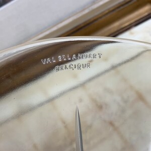May include: Close-up of a clear glass plate with the inscription "VAL ST LAMBERT BELGIQUE" etched on the bottom.